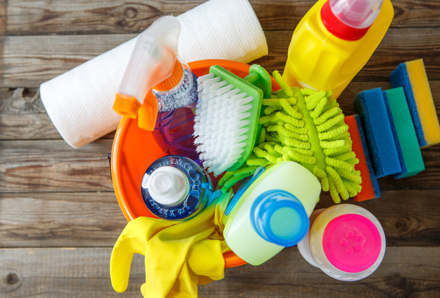 Plastic bucket with cleaning supplies on wood background