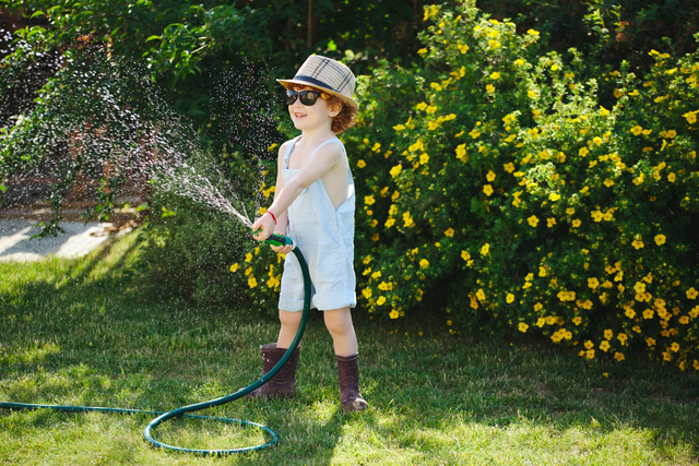 cute little boy watering the garden with hose