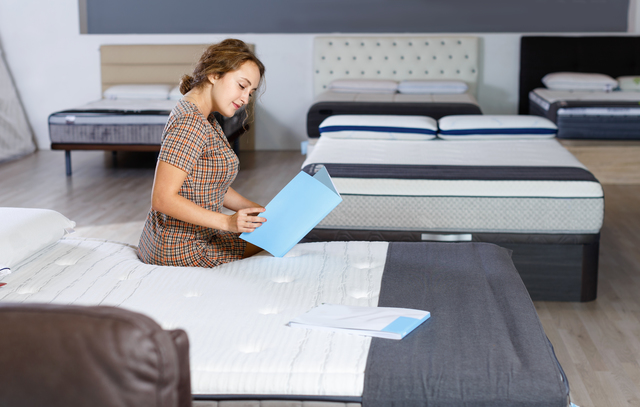 Young happy cheerful positive  attractive woman choosing right mattress with booklet in home furnishings store