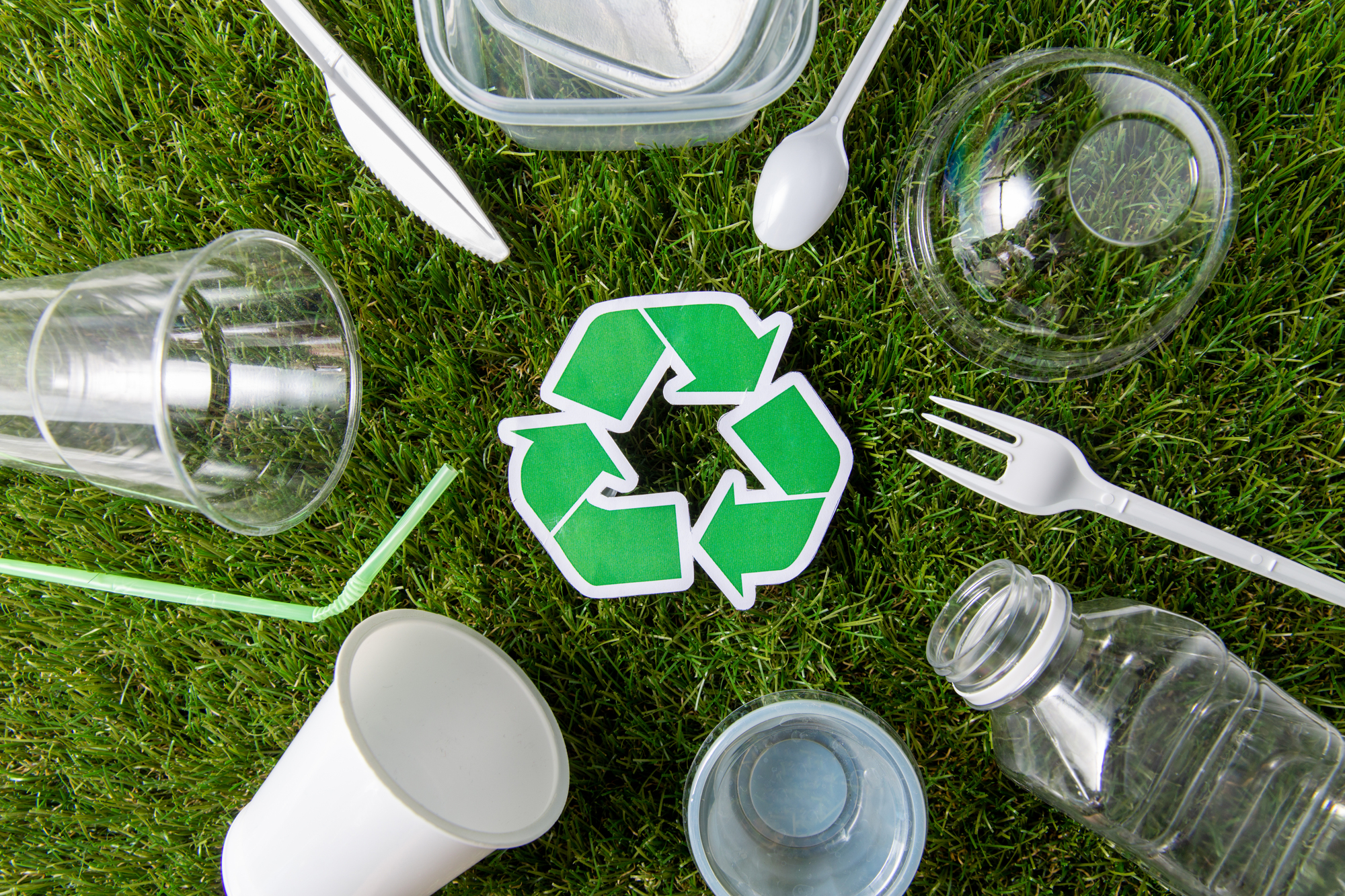 environment, sustainability and ecology concept - close up of green recycling sign and plastic waste on grass